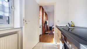 A modern kitchen with a stainless steel range hood, a window with blinds, and a view into a bedroom with a bed and curtains. - Apartment "Apartment in Hannover Mitte" with Wi-Fi (Hannover)