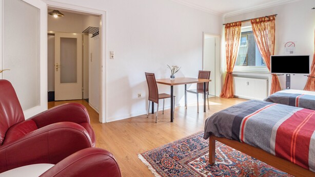 A bedroom with a bed, a desk, two chairs, a TV, and a door leading to another room. - Apartment "Apartment in Hannover Mitte" with Wi-Fi (Hannover)