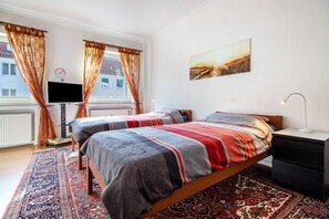 Une chambre avec deux lits, une télévision, une table de chevet et une grande fenêtre avec des rideaux.