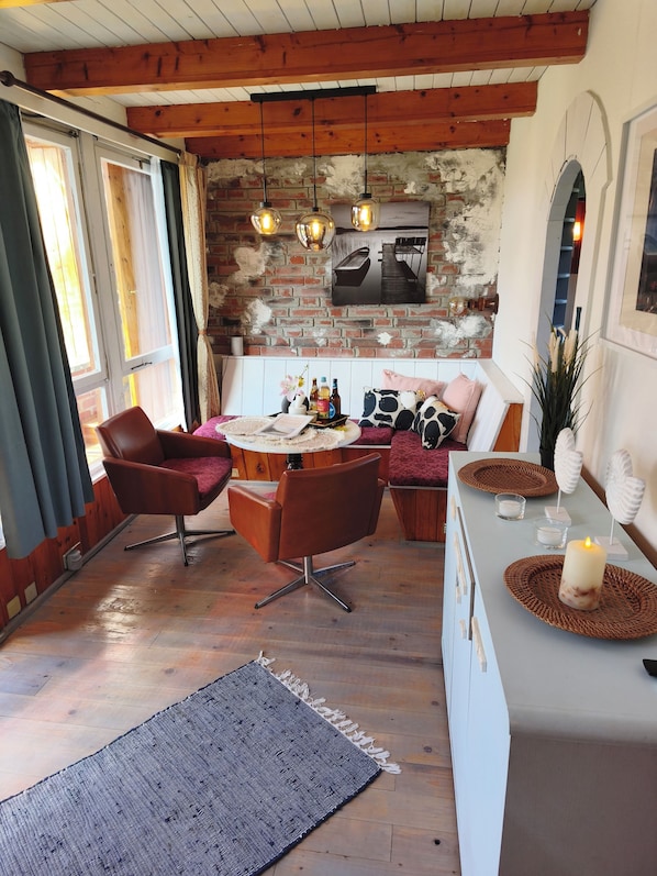 A cozy room with a wooden ceiling, a brick wall, a dining table with chairs, and a bar area with a candle.