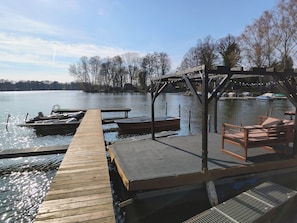 A wooden dock extending into a calm lake with boats docked, a covered seating area, and a clear view of the surrounding trees.