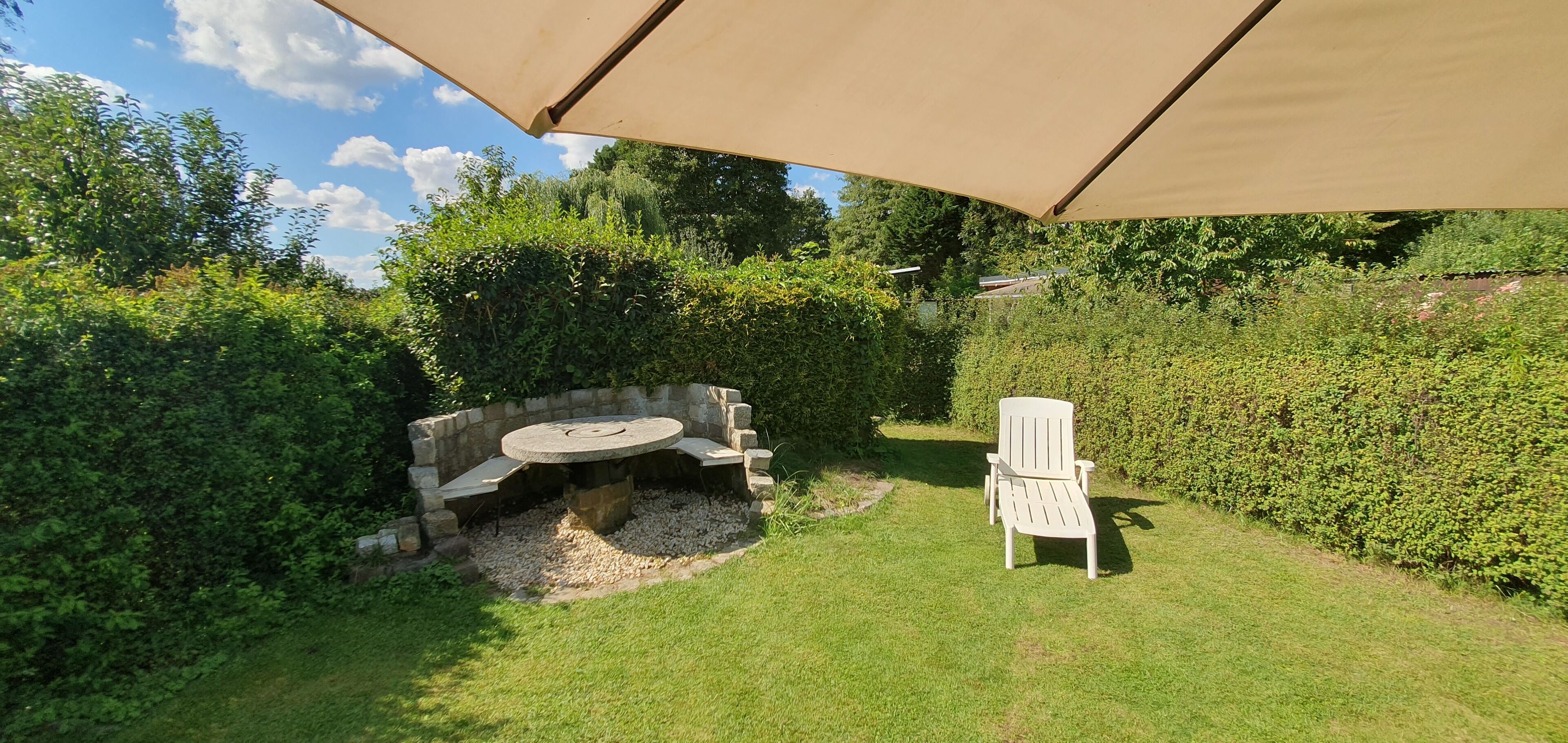 A patio with a stone fire pit, a white chair, and a large umbrella providing shade.