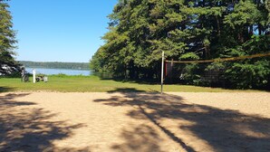 Un terrain de volley-ball avec un filet, entouré d’arbres et bordé par un lac.