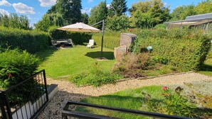 Un jardin bien entretenu, agrémenté d’un espace détente, d’une table de patio et d’un grand parasol.