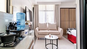 Habitació d'hotel compacta amb cuineta, un sofà, una taula rodona petita, un dispensador d'aigua i un llit amb llençol vermell.