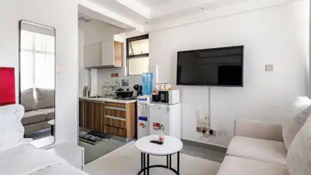 Un saló modern amb un sofà, una taula de centre, una televisió de pantalla plana i una zona de cuina amb armaris i electrodomèstics.