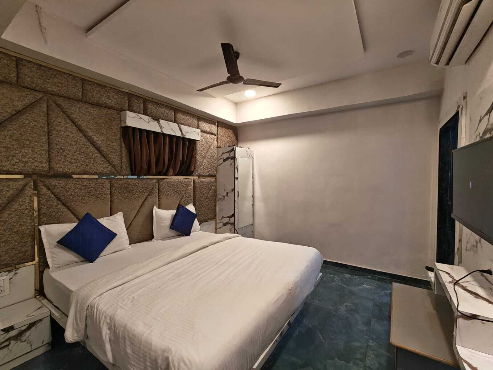 Une chambre à coucher avec un lit, un ventilateur de plafond, une télévision et un mur décoré d’un motif imitant le marbre.