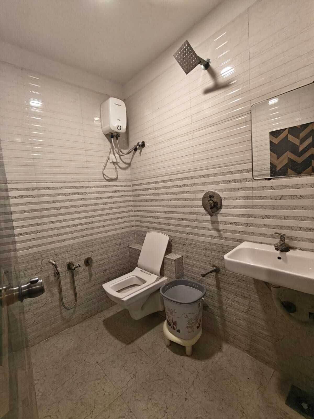 A bathroom with a toilet, bidet, shower, sink, and a trash bin.