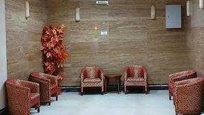 A lobby with a patterned wall, a decorative plant, and a seating area with patterned chairs and a small table.