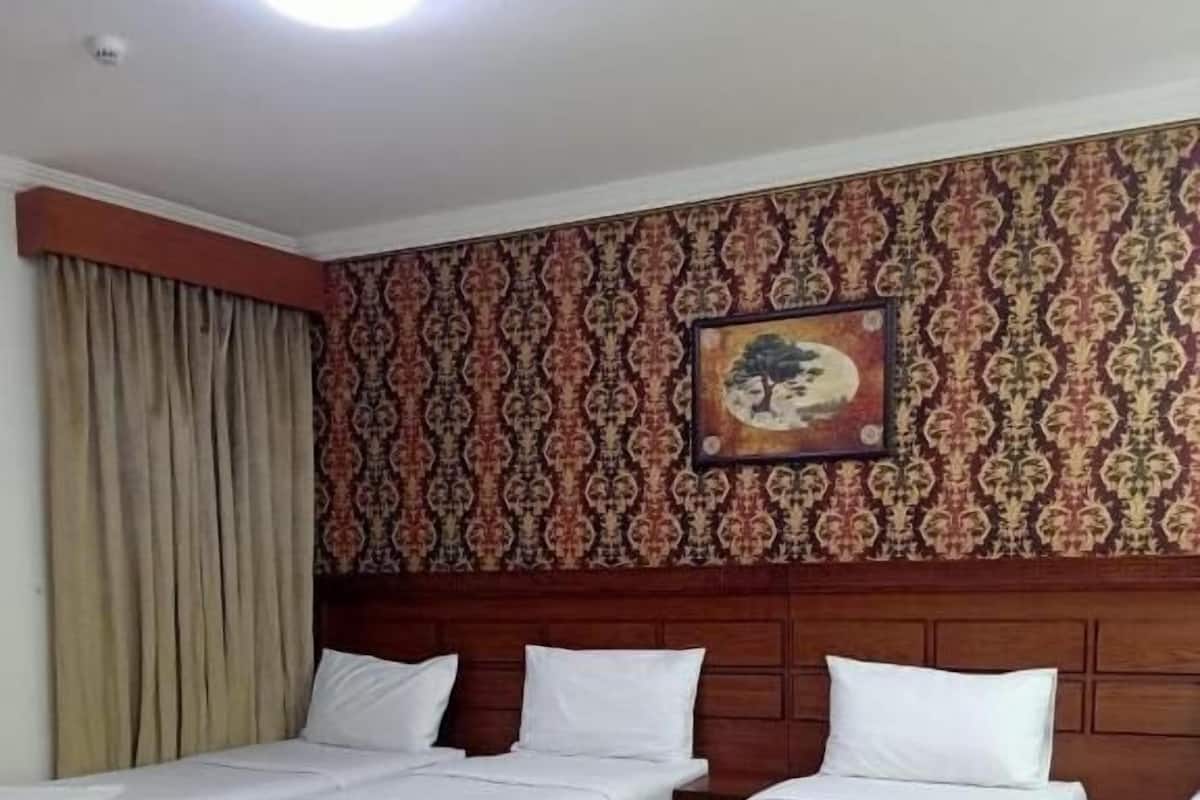 A hotel room with three single beds, a patterned wallpaper, a ceiling light, and a framed picture on the wall.