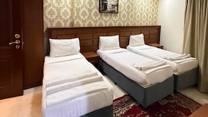 A hotel room with two beds, a wooden wardrobe, a patterned wall, and a ceiling light fixture.