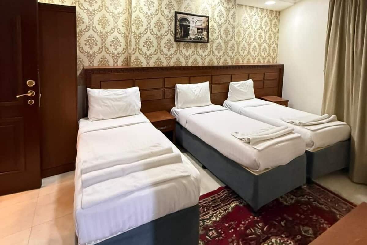 A hotel room with two beds, a wooden wardrobe, a patterned wall, and a ceiling light fixture.
