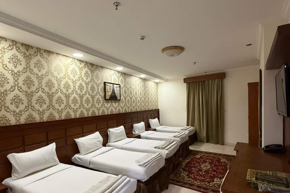 A hotel room with four beds arranged in a row, a wooden headboard, a television on a wooden table, and a patterned wallpaper.