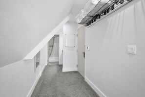 En smal gang med hvide vægge, gråt gulvtæppe og et skråt loft.