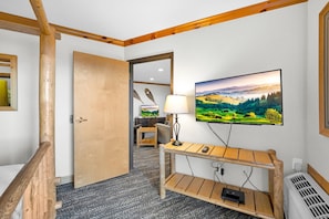 A hotel room with a wooden bench, a TV mounted on the wall, a door, and a carpeted floor.