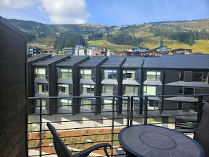 A modern building with multiple balconies, a view of a mountainous landscape, and a clear sky.