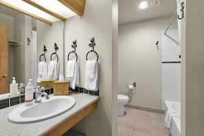 Ein Badezimmer mit Waschbecken, Spiegel, Handtuchhaken, Toilette und Duschbereich.
