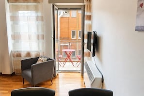 A hotel room with a sofa, a small table, a TV mounted on the wall, and a view of the outside balcony. - Style Homes (Milan)
