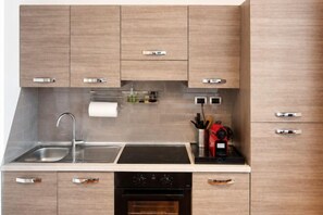 A modern kitchen with a stainless steel sink, black stove, and wooden cabinets. - Style Homes (Milan)