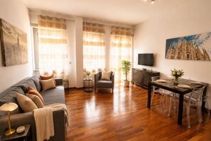 A living room with a sofa, dining table, chairs, a TV, and artwork on the walls. - Style Homes (Milan)