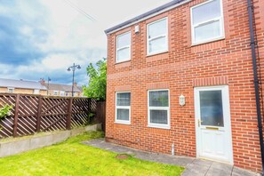A two-story brick house with a white door and windows, a fenced backyard, and a clear sky. - Toast Stays - The Peth House (Shildon)