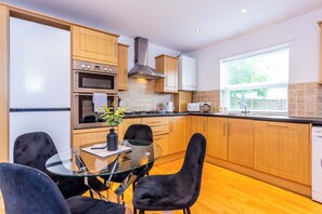 A modern kitchen with wooden cabinets, a glass dining table, and black chairs. - Toast Stays - The Peth House (Shildon)