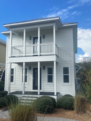 A two-story building with a balcony, a front door, and a number '153' on the side. - The Beach Calls (Santa Rosa Beach)