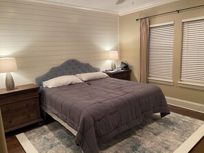 A neatly made bed with a headboard, two bedside tables with lamps, and a window with blinds. - The Beach Calls (Santa Rosa Beach)