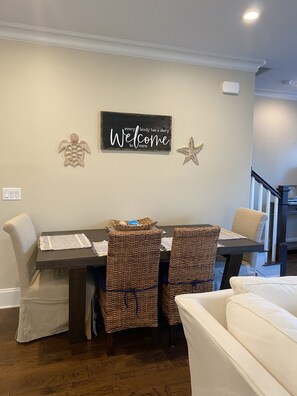 A dining area with a table and chairs, a welcome sign, and decorative starfish on the wall. - The Beach Calls (Santa Rosa Beach)