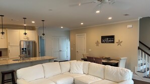 A modern kitchen with a built-in refrigerator, a dining area with a table and chairs, and a living room with a sectional sofa.