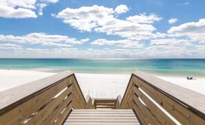 A wooden boardwalk leading to a beach with clear turquoise water and a partly cloudy sky. - The Beach Calls (Santa Rosa Beach)