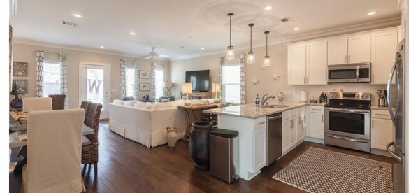 A modern kitchen with white cabinets, stainless steel appliances, and a dining area with a sofa and chairs. - The Beach Calls (Santa Rosa Beach)