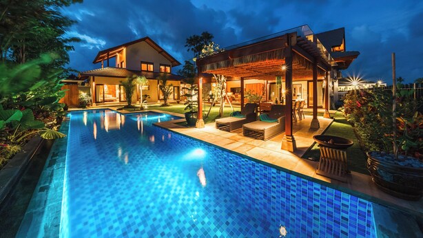 Una casa moderna con piscina, mobiliario exterior y un patio cubierto.
