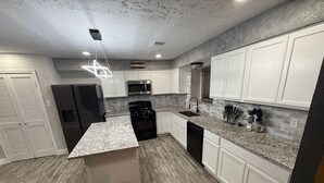 Una cocina moderna con armarios blancos, encimeras de granito, un refrigerador de acero inoxidable, un microondas y un lavavajillas.
