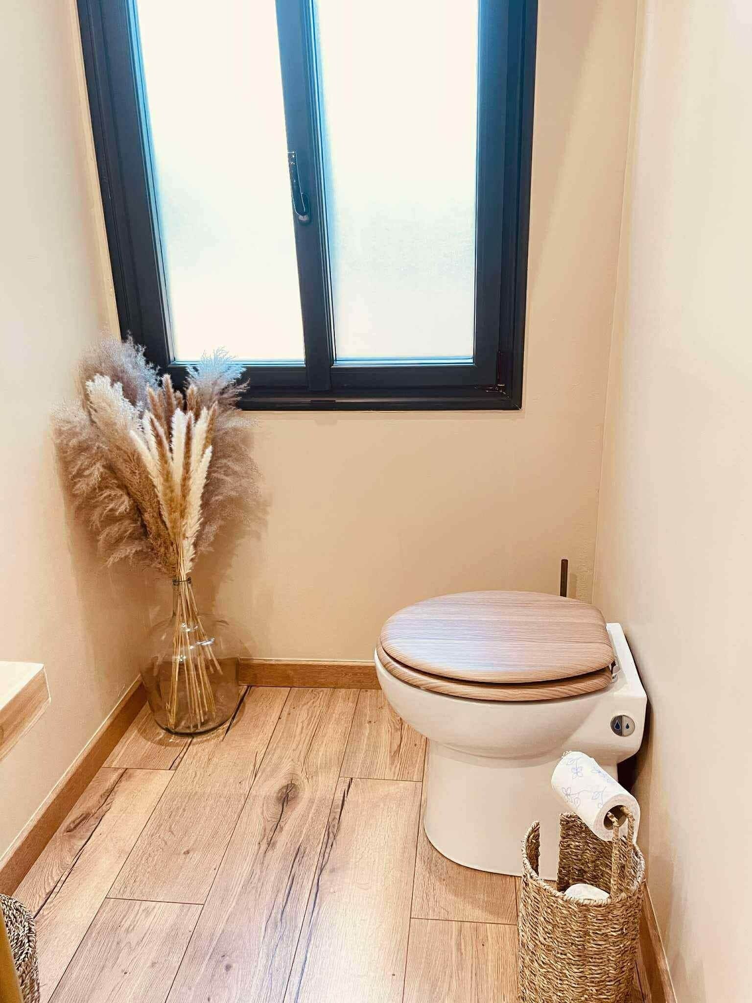 A small bathroom with a toilet, a window, and a wicker basket with toilet paper.