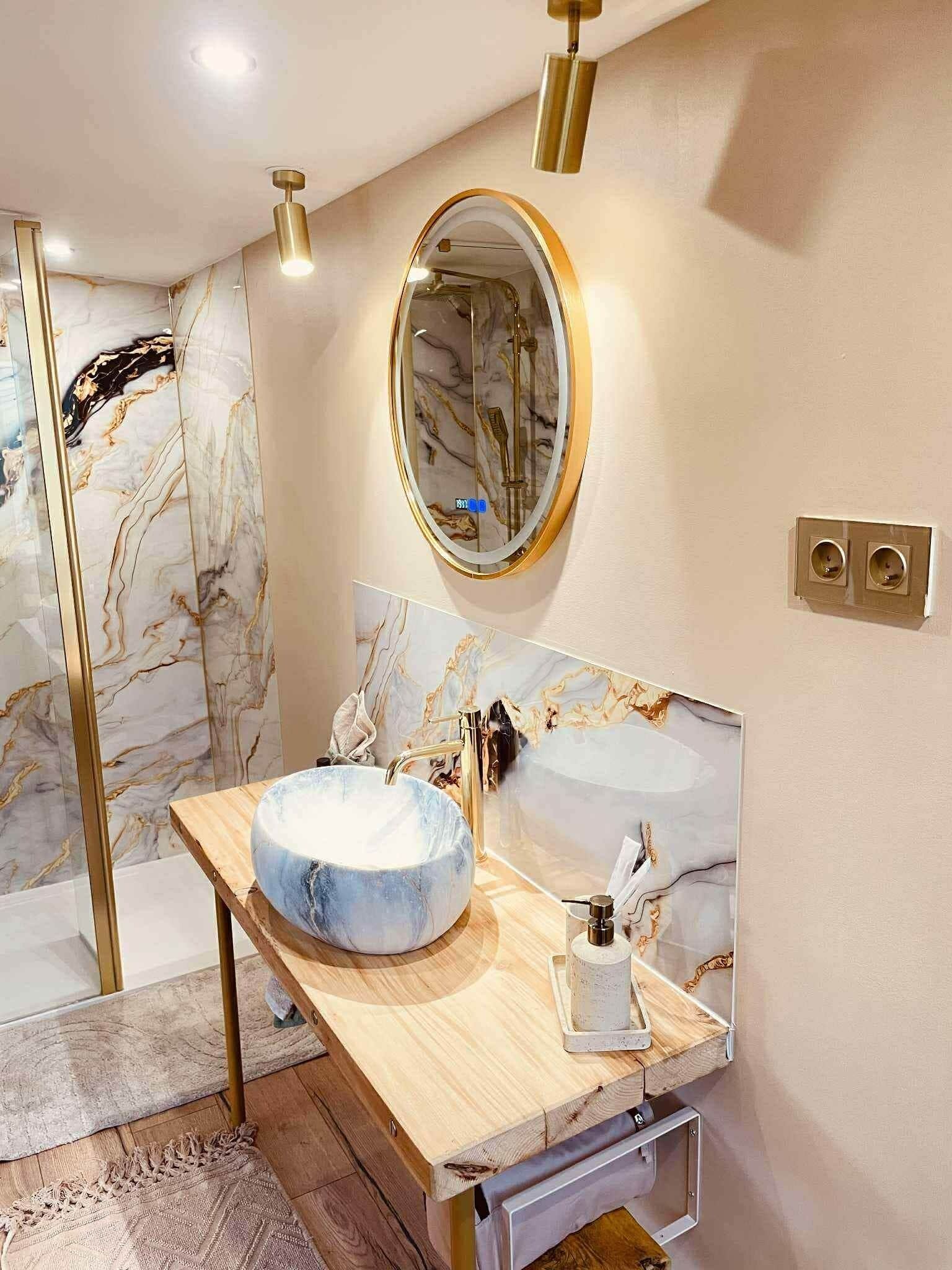 Une salle de bain avec un meuble-lavabo en marbre, un miroir rond et une cabine de douche en verre.