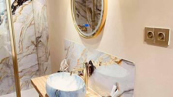 Une salle de bain avec un meuble-lavabo en marbre, un miroir rond et une cabine de douche en verre.