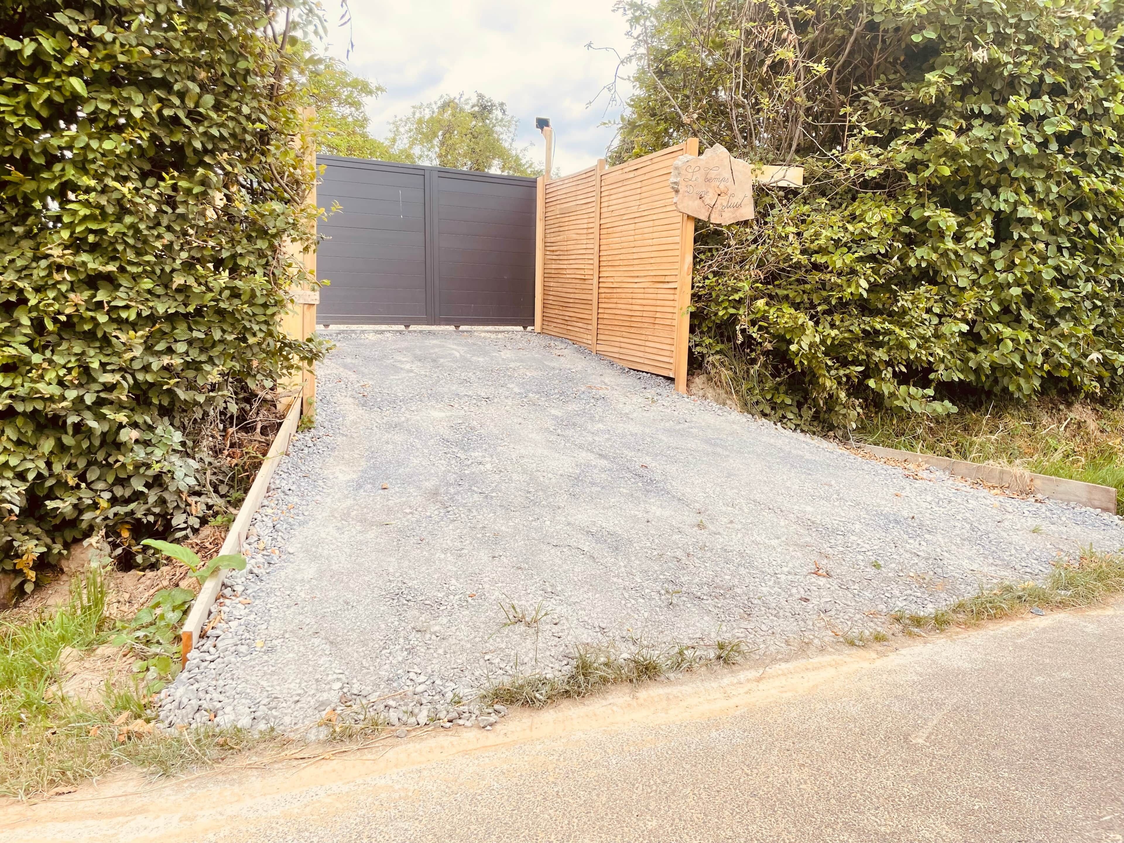 A gravel driveway leading to a wooden gate with a black fence.