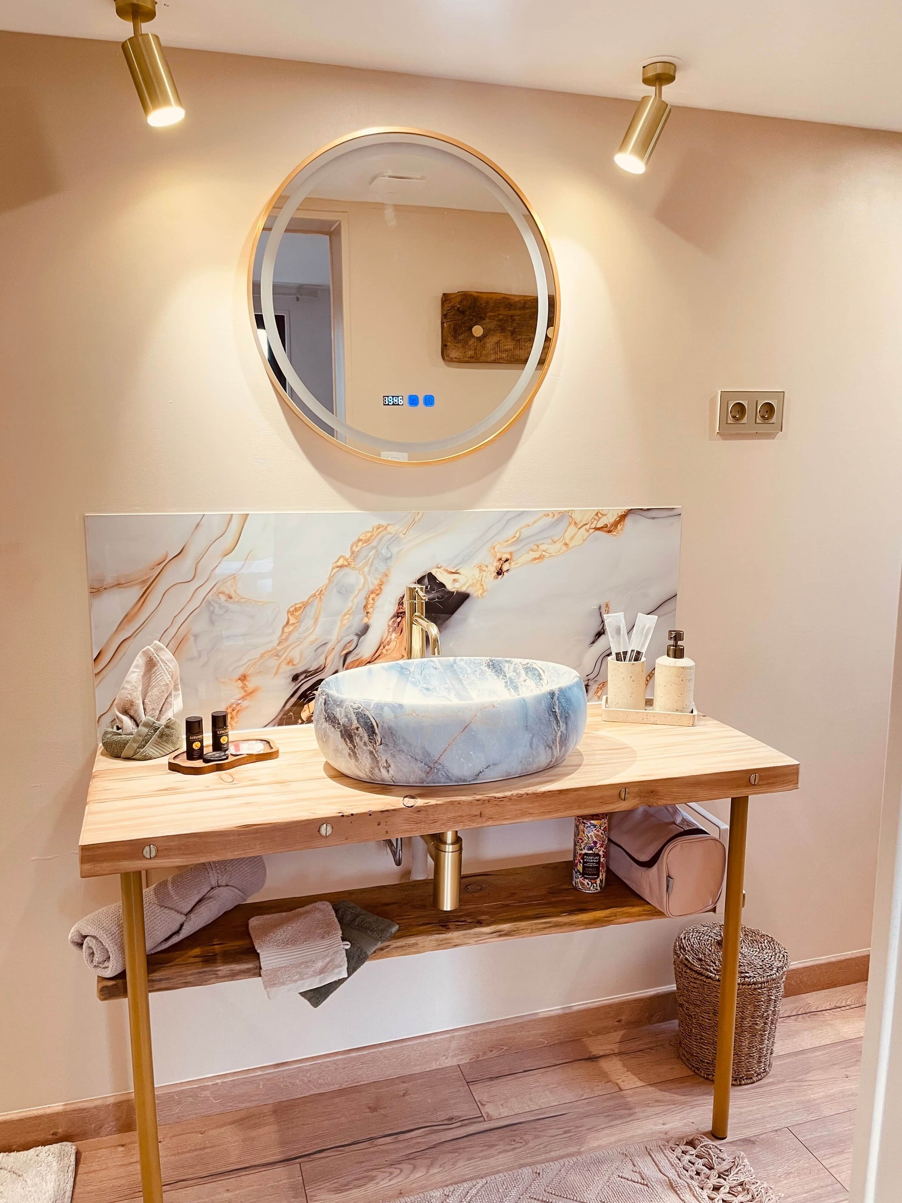 A bathroom with a marble vanity, a round mirror, and a wooden shelf.