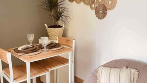 A dining area with a wooden table set for two, a potted plant, and a wall-mounted decorative piece. - Le Temps d'une Nuit (Landouzy-la-Ville)