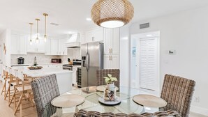 A modern kitchen with white cabinets, stainless steel appliances, and a glass dining table surrounded by wicker chairs.