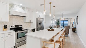 A modern kitchen with white cabinetry, stainless steel appliances, and a central island with bar stools.