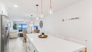 A modern kitchen with a white island, pendant lights, and a view of the ocean.