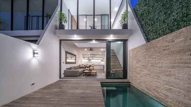 Et moderne hus med en træterrasse, en glasdør til en stue og en swimmingpool.