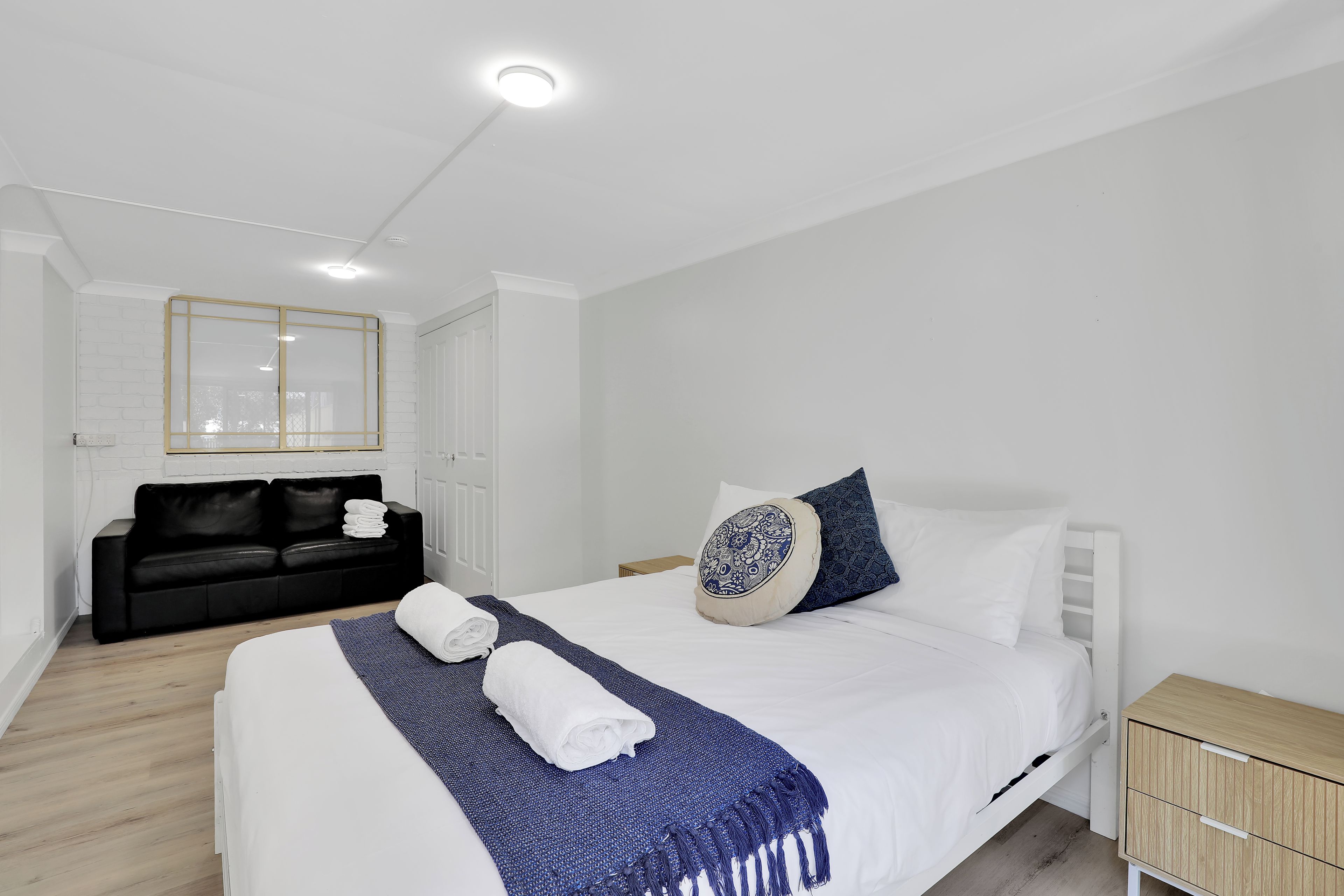 Ein modernes Schlafzimmer mit einem großen Bett, einem schwarzen Sofa, einem Nachttisch aus Holz und einem Spiegel an der Wand.