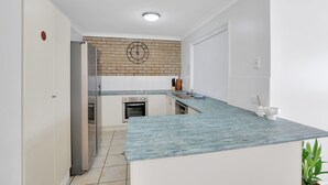 A modern kitchen with a blue marble countertop, a brick backsplash, and white cabinetry.