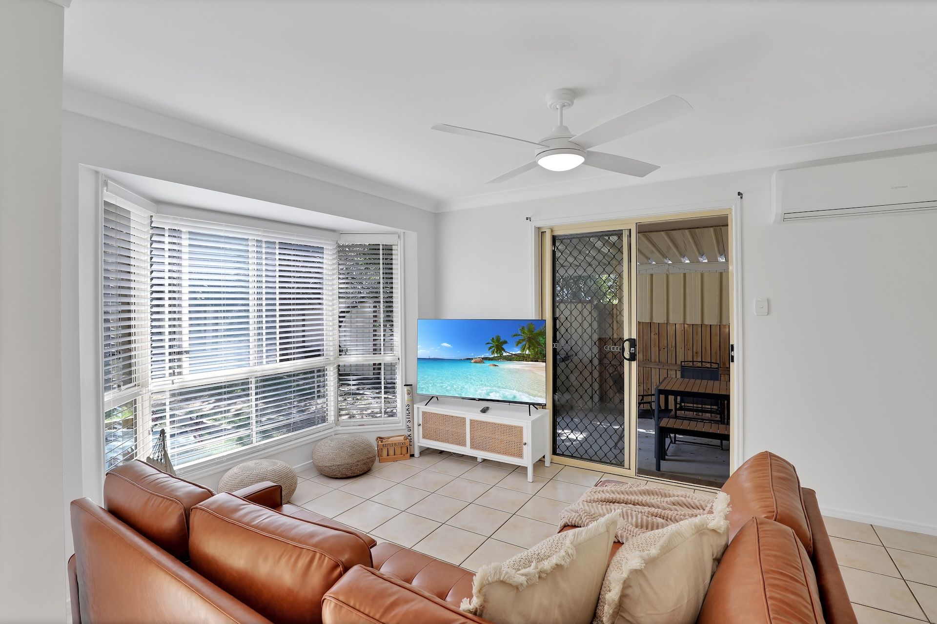 Un salon avec un canapé en cuir, un téléviseur et une vue sur la plage, accessible par une porte coulissante.