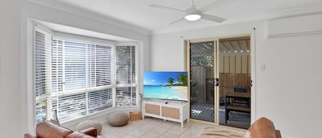 A living room with a leather sofa, a television, and a view of a beach through a sliding door.