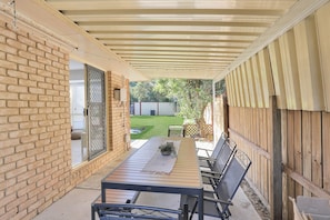 Une terrasse couverte avec une table et des chaises, des murs en briques et une clôture en bois.