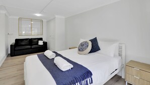 A modern bedroom with a large bed, a black sofa, a wooden nightstand, and a mirror on the wall.